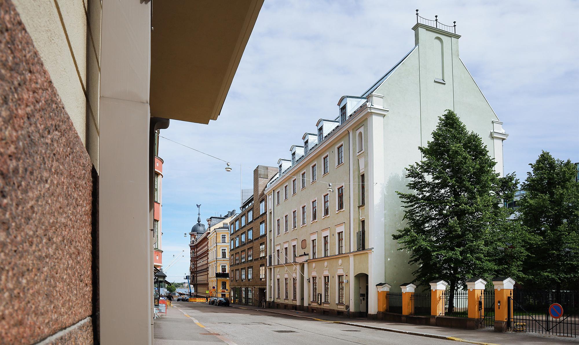 Kaupungin katu, jonka varrella on suuri, vaaleanvihreä rakennus, jossa on ikkunoita viidessä kerroksessa. 