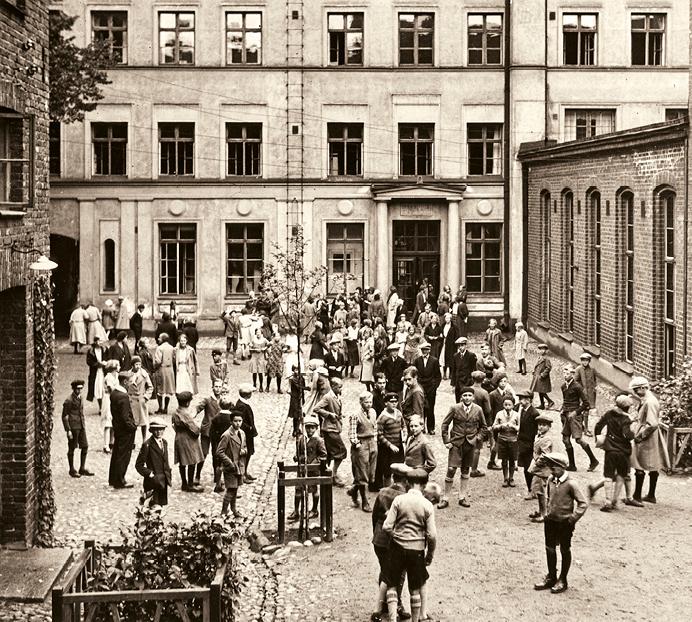 Mustavalkoinen valokuva koululaisista rakennuksen pihalla.